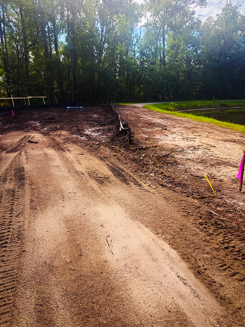 Wide view of a prepared property access route beside a pond and wooded site