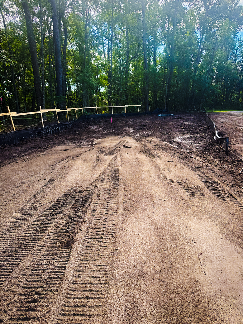 Prepared sandy access path with equipment tracks leading into a wooded job site